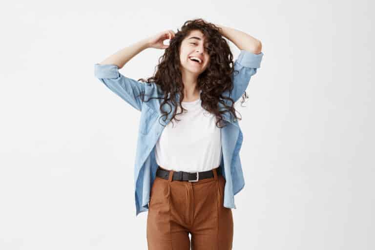 Good-looking emotional female model wearing long wavy hair loose has charming pleasant broad smile, looks happily at camera, dreams about vacations with boyfriend